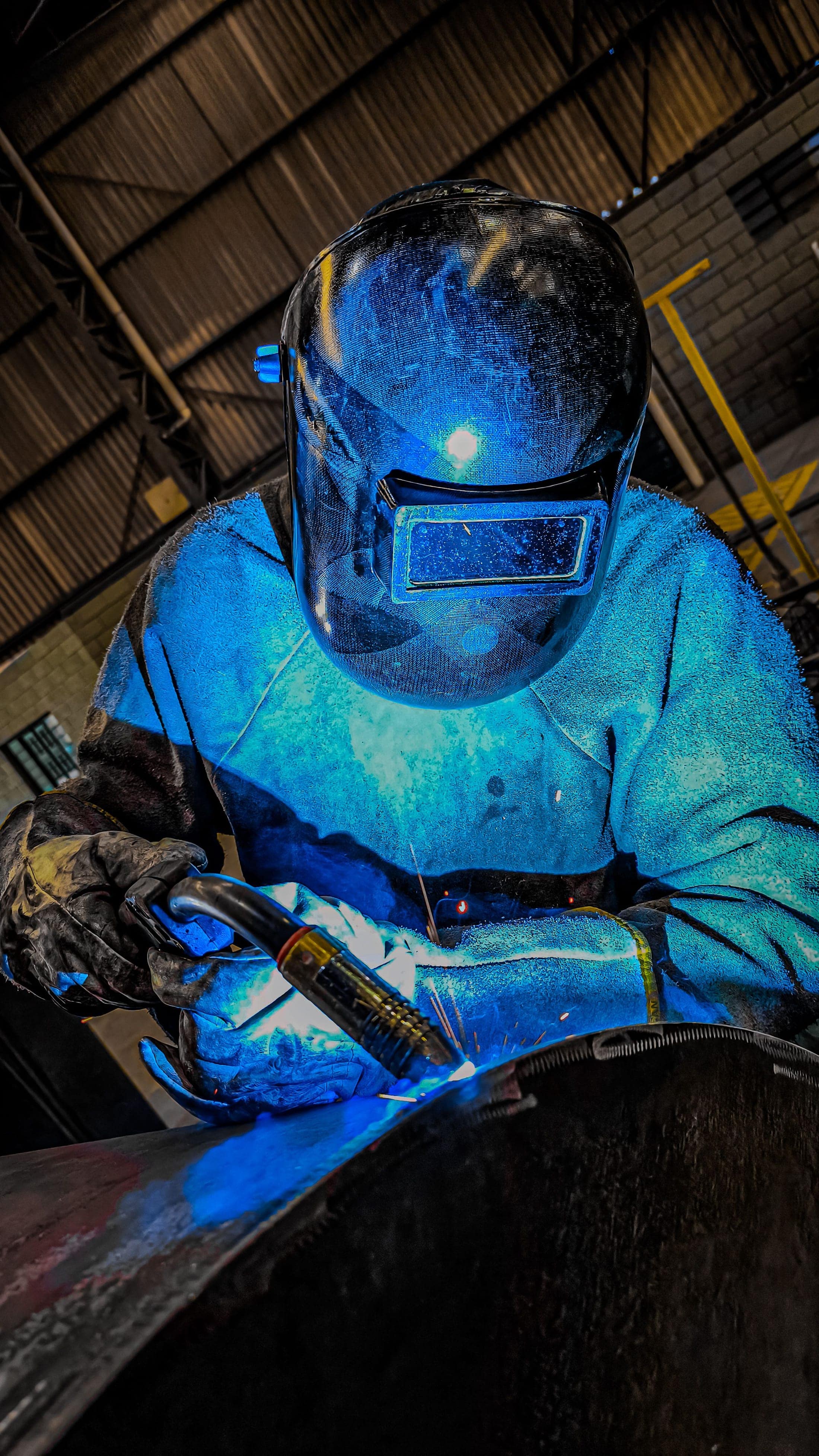Welder in protective helmet and leathers working at a bench