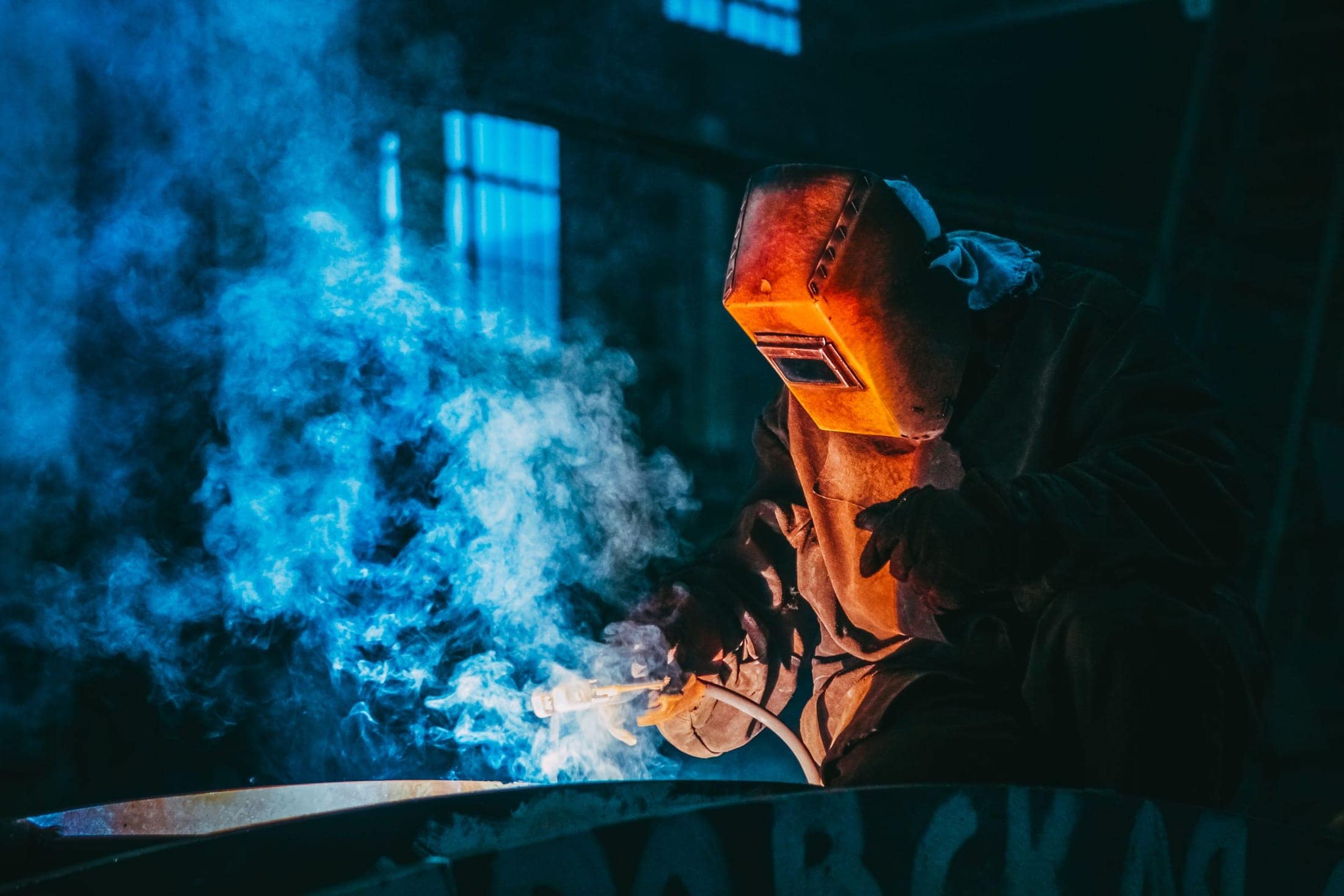 Welder working through smoke, lit by the arc