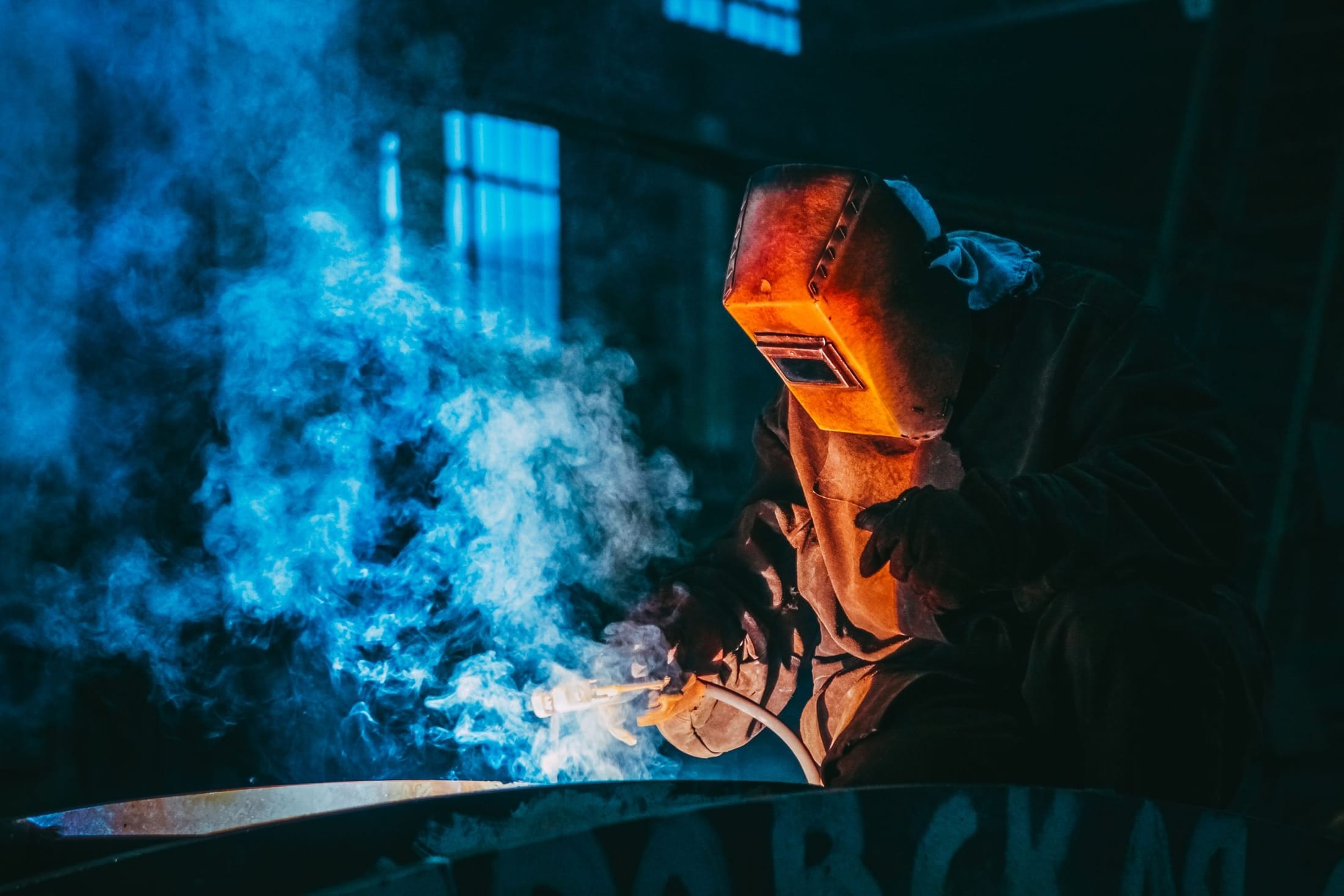 Welder working through smoke, lit by the arc